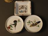 three plates with birds painted on them sitting on a table