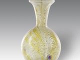 vase en verre jaune et blanc sur fond gris, orné d'un œil rouge