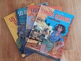 three books are sitting on a wooden table, one is a comic book and the other is a comic book