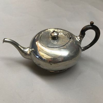 une théière ancienne en argent posée sur une nappe blanche, avec une anse noire