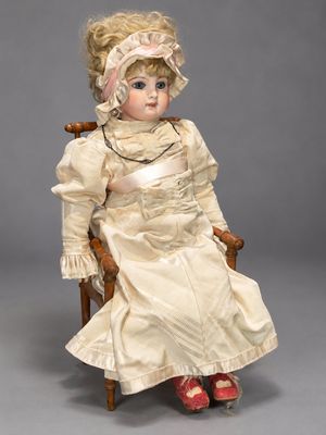 an antique doll sitting in a chair wearing a white dress and red shoes
