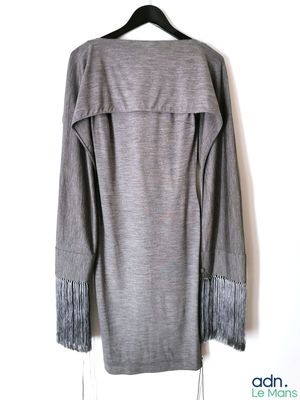 un pull gris à franges suspendu à un cintre devant un mur blanc