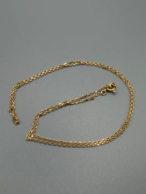 un collier en or avec une chaîne posée sur une surface grise