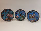 three plates with flowers and birds on them sitting on a white surface