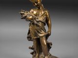 une statue en bronze représentant un garçon tenant un oiseau, posée sur un socle