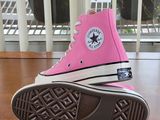 pink converses are sitting on a wooden table with a plant in the background