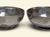 two silver bowls sitting next to each other on a table