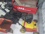 deux tondeuses à gazon posées par terre à côté d'un chariot rouge
