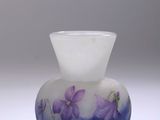 un vase en verre orné de fleurs violettes, posé sur une surface blanche