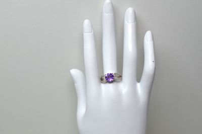 une image représentant la main d'une femme tenant une bague sertie d'une pierre violette