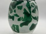 un vase vert et blanc posé sur une surface blanche