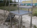 a metal table and stairs in the sand near a building