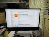 un écran d'ordinateur posé sur un bureau, à côté d'une pile de papiers