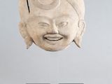 une photo représentant une sculpture représentant le visage d'un homme, posée sur un socle à côté d'un fruit