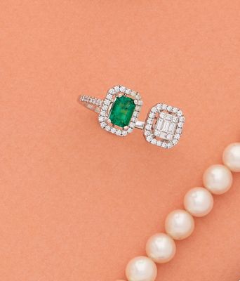 un gros plan sur un collier de perles accompagné d'une bague sertie d'une émeraude et de diamants