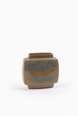 un petit vase marron et vert posé sur une surface blanche