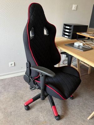 une chaise de bureau noire et rouge devant un bureau d'ordinateur