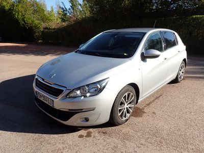 La voiture blanche est garée sur le parking, près des buissons.