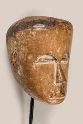 une photo représentant un masque en bois posé sur un socle devant un mur blanc