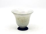 un petit bol en verre avec un socle noir posé sur une surface blanche