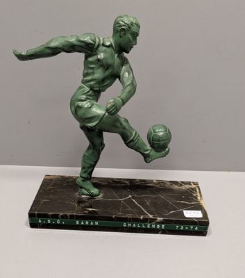 statue of a man kicking a soccer ball on a marble base