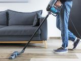 un homme en train de nettoyer le sol du salon à l'aide d'un aspirateur filaire