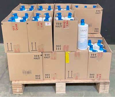 Plusieurs cartons d'eau sont empilés sur une palette devant un mur noir