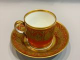 an orange and gold cup and saucer sitting on top of a white table