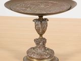 une image représentant une assiette en bronze posée sur une table en bois, sur laquelle se trouve un oiseau