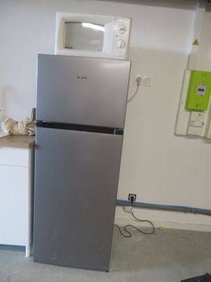 a silver refrigerator in a kitchen with a microwave on top of it