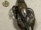 une petite statue représentant un homard, posée par terre à côté d'une pièce de monnaie