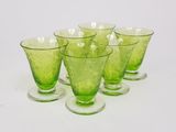 six green glass goblets are lined up on a white surface