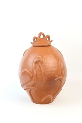 un vase marron muni d'un couvercle, posé sur une surface blanche