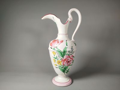 un vase blanc muni d'une anse rose et orné d'un motif floral