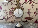 a clock that is on a table in front of a painting
