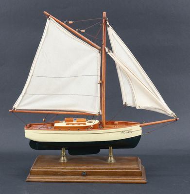 maquette en bois d'un voilier aux voiles blanches, posée sur un socle en bois