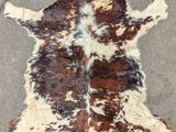 tapis en peau de vache marron et blanche posé sur un sol en béton