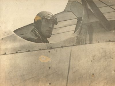 an old photo of a man in a pilot ' s helmet looking out the window of a plane