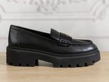 a close up of a black loafer shoe on a wooden table