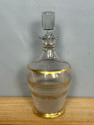 une bouteille en verre transparent à bord doré posée sur une table en bois