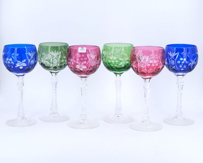 plusieurs verres à vin de différentes couleurs alignés en rang sur une surface blanche