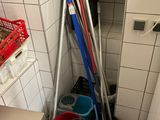 several brooms and buckets are lined up against a wall in a bathroom