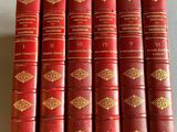 six livres en cuir rouge aux tranches dorées, posés sur un fond blanc
