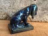 statue d'un chien assis sur une table en bois près d'un mur en pierre
