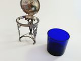 a blue glass next to a silver plate on a table