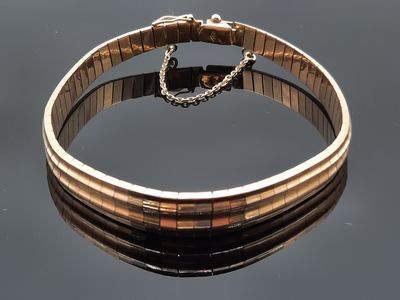 bracelet en or avec une chaîne et un fermoir posé sur une surface réfléchissante