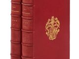 trois livres rouges ornés d'emblèmes dorés, posés sur une surface blanche