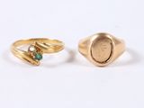 two gold rings with emerald stones on them on a white surface