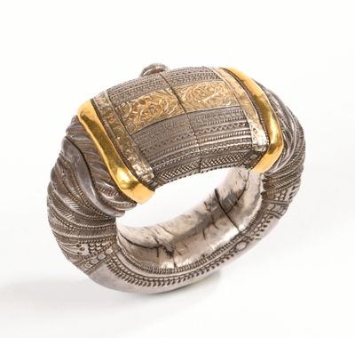 un gros plan d'un bracelet en argent rehaussé de touches dorées sur fond blanc