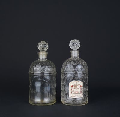deux bouteilles en verre transparent avec des bouchons argentés, posées sur une surface noire